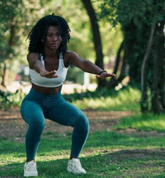 retrato de mujer negra con ropa deportiva, haciendo ejercicios de sentadilla, en un parque con luz natural. concentrada para hacer deporte