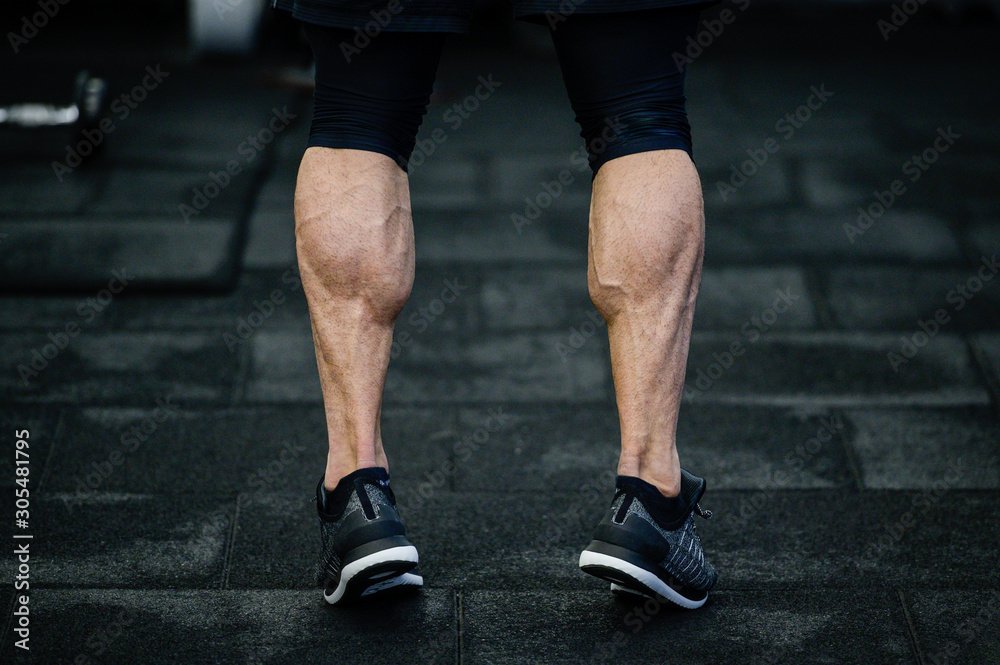 trained legs with muscular calves in sneakers in training gym during hard fitness and crossfit workout